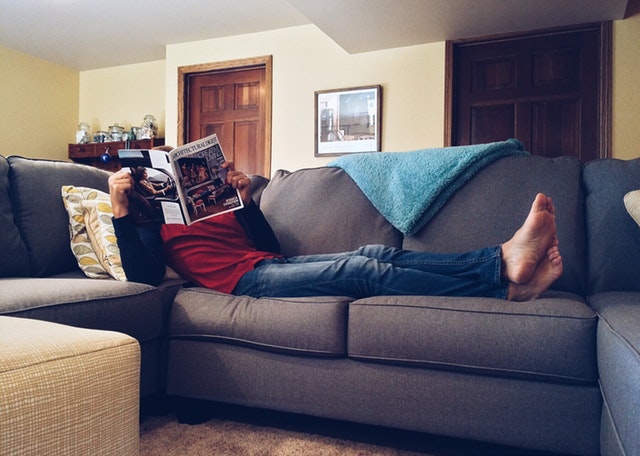 Muž ležící na pohovce a čtoucí noviny
